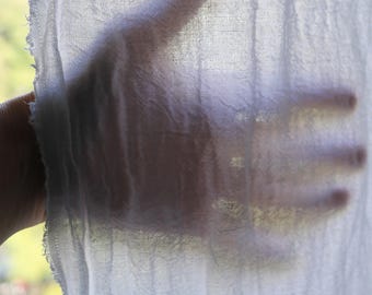 Könnte beinhalten: Ein durchscheinender, weißer, leichter Stoff mit sichtbarem Gewebe und einer rohen, ausgefransten Kante. Das Material ist lichtdurchlässig und lässt die Silhouette einer Hand erkennen, die hinter der Textiloberfläche liegt.