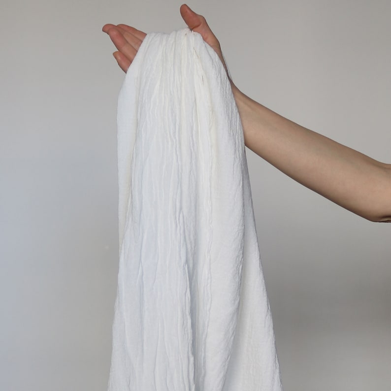 May include: A white, crinkled fabric scarf being held by a hand.