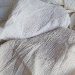 Puede incluir: Primer plano de una tela de algod&oacute;n blanca con textura arrugada. La tela es suave y ligera, y tiene un aspecto natural y sin blanquear.
