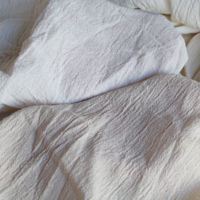 Puede incluir: Primer plano de una tela de algod&oacute;n blanca con textura arrugada. La tela es suave y ligera, y tiene un aspecto natural y sin blanquear.