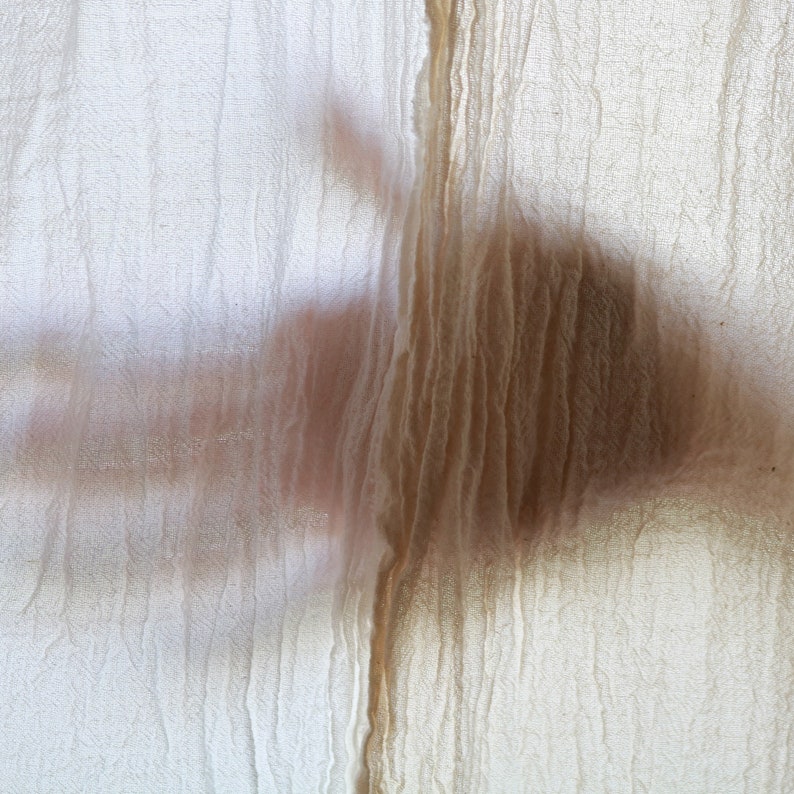 May include: A close-up of a sheer white fabric with a textured surface. The fabric is draped over a surface, creating a shadow of a hand.