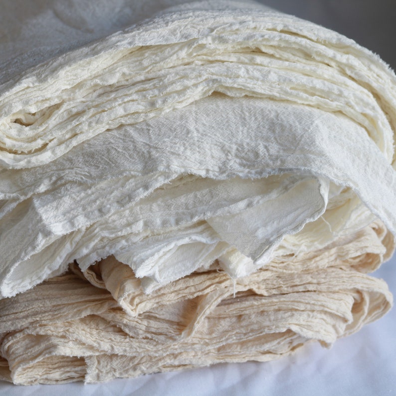 May include: A stack of white and cream colored fabric, folded and layered, with a rough, textured surface.