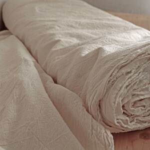 May include: Two rolls of off-white fabric with a textured surface. The fabric is rolled up and the edges are frayed.