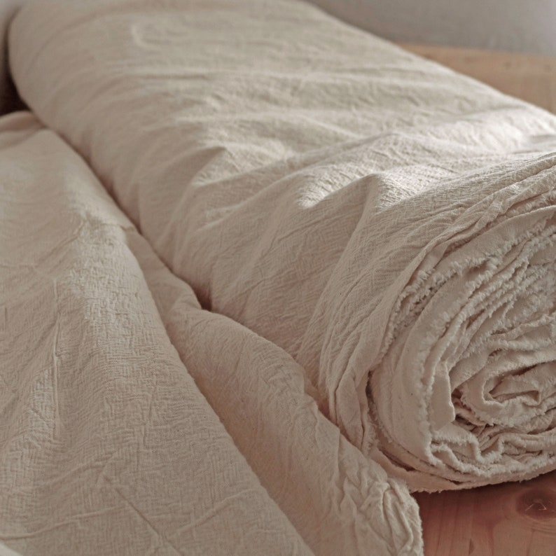 May include: Two rolls of off-white fabric with a textured surface. The fabric is rolled up and the edges are frayed.