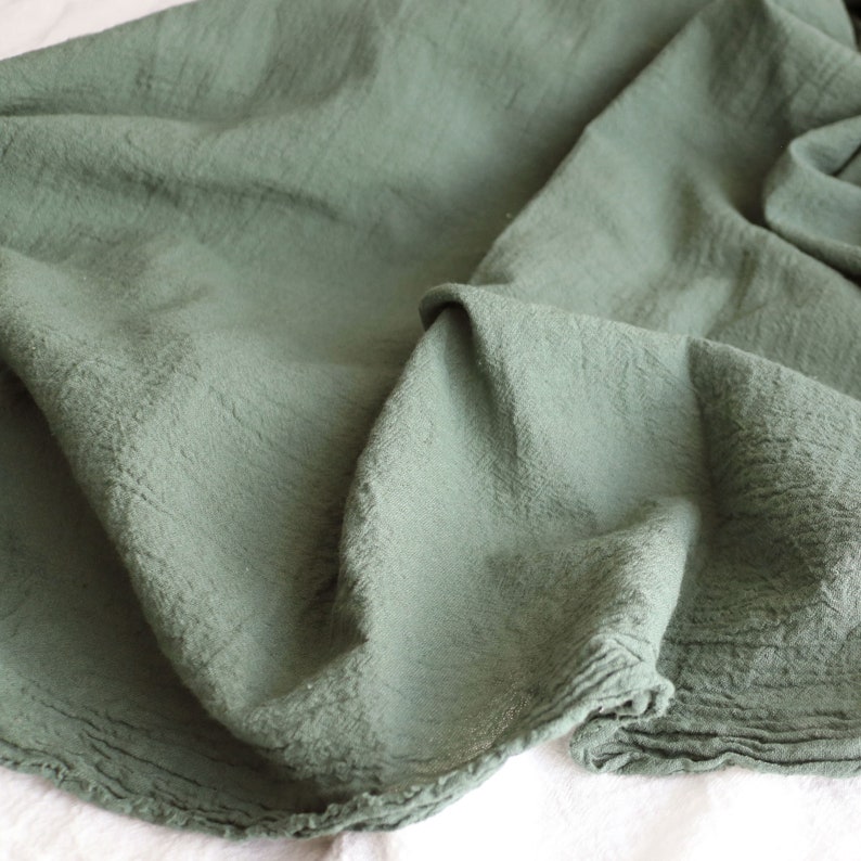 May include: A soft, green fabric with a slightly textured surface. The fabric is folded and draped, showing its texture and drape.