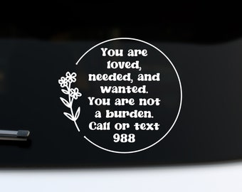 Könnte beinhalten: Weißer Vinyl-Aufkleber mit einem runden Design, das ein florales Motiv und den Text "You are loved, needed, and wanted. You are not a burden. Call or text 988." zeigt.