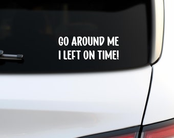 May include: White vinyl sticker with the text "Go around me I left on time!" on a black background. The sticker is on the back window of a white car.