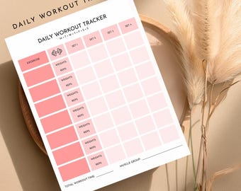 May include: A white and pink Daily Workout Tracker sheet with sections for exercise, weights, reps, and sets. The top of the sheet reads "DAILY WORKOUT TRACKER" and "M-T-W-T-F-S-S". The sheet is on a wooden tray with dried plants.