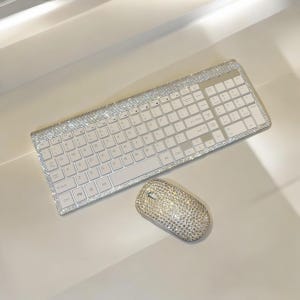 Könnte beinhalten: Eine weiße drahtlose Tastatur und Maus, die mit funkelnden Strasssteinen besetzt sind. Die Tastatur hat ein Standardlayout mit Funktionstasten und einem Nummernblock. Die Maus ist in Standardgröße mit einem Scrollrad.
