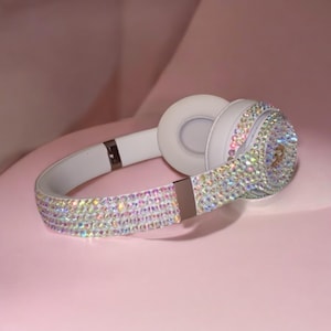 May include: White headphones with a crystal-like design. The headphones are covered in iridescent rhinestones.