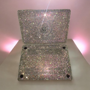 May include: A laptop computer covered in iridescent rhinestones. The laptop is closed and the lid is decorated with a pattern of small, sparkling crystals.