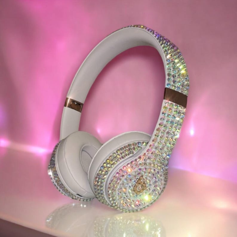 May include: White over-ear headphones with a gold band and covered in iridescent rhinestones.