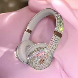 May include: White wireless headphones with a crystal-like design. The headphones are covered in iridescent rhinestones.