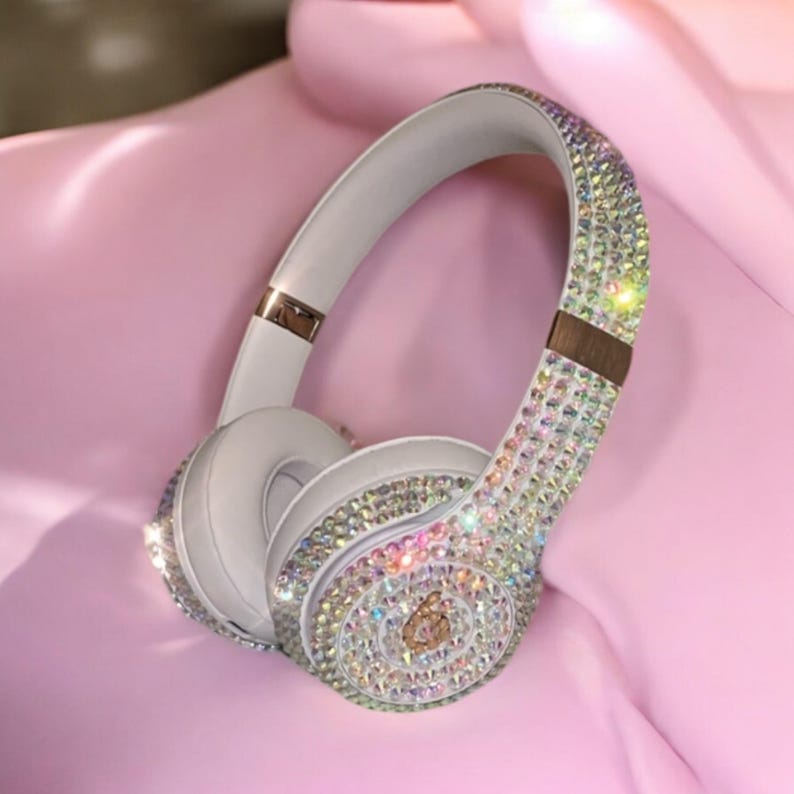 May include: White wireless headphones with a crystal-like design. The headphones are covered in iridescent rhinestones.
