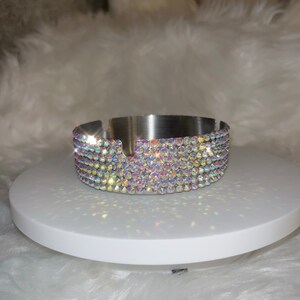 May include: A silver ashtray with a round, flat base and a rim decorated with iridescent rhinestones.
