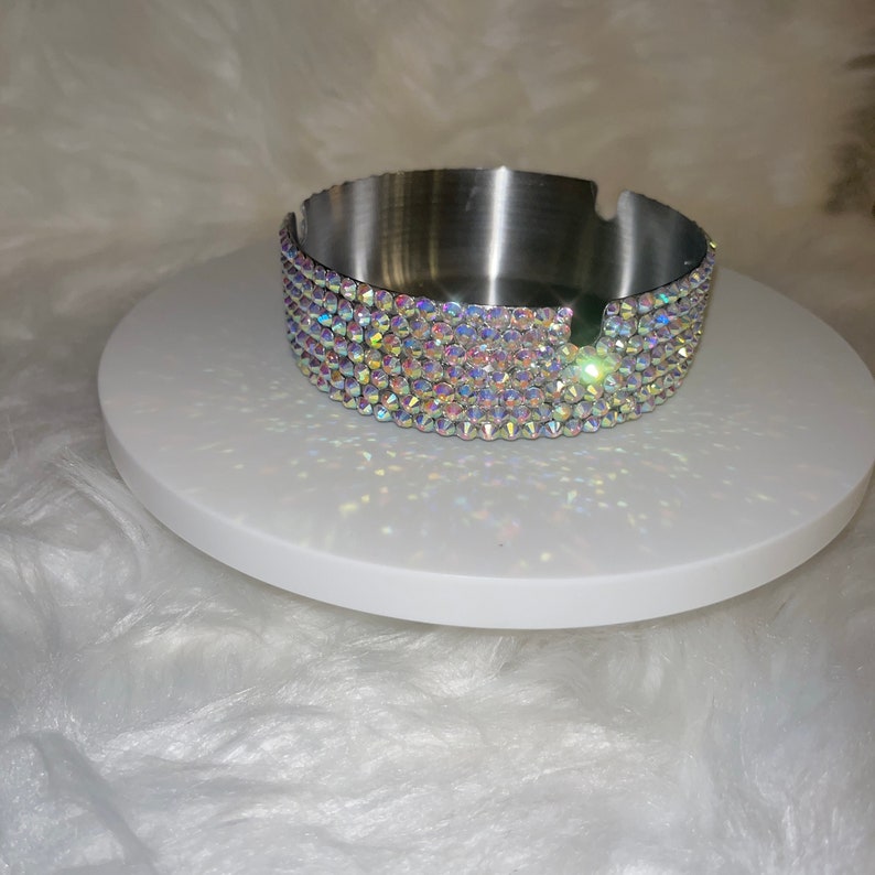 May include: A silver ashtray with a decorative band of iridescent rhinestones around the top edge.