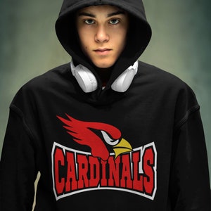 以下が含まれることがあります： 赤いカーディナルのロゴと白い文字で「CARDINALS」と書かれた黒いフード付きスウェットシャツ。首に白いヘッドホンをかけています。
