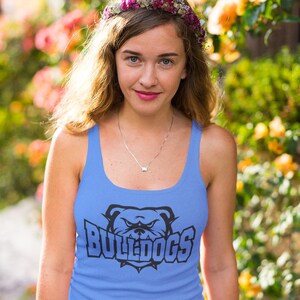 Op de afbeelding: Een vrouw draagt een lichtblauw tanktop met een zwarte bulldog-afbeelding en de tekst "BULLDOGS". Ze draagt een bloemenkrans en glimlacht naar de camera.
