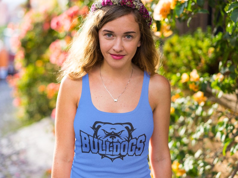 Op de afbeelding: Een vrouw draagt een lichtblauw tanktop met een zwarte bulldog-afbeelding en de tekst "BULLDOGS". Ze draagt een bloemenkrans en glimlacht naar de camera.
