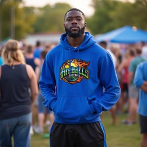 May include: A royal blue hoodie with the text "Fireballs Softball" in a colorful graphic. The hoodie has a front pocket and a drawstring hood. The person is wearing black shorts.