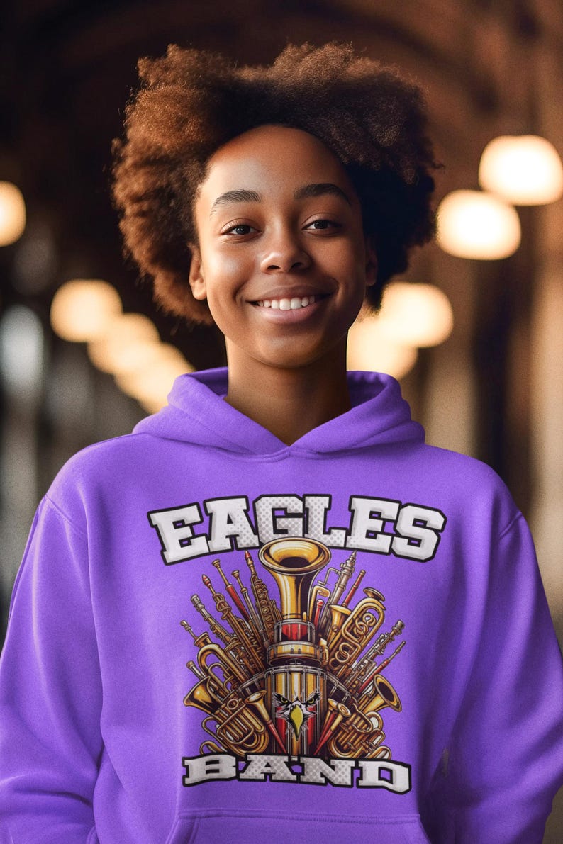 K&ouml;nnte beinhalten: Lilafarbener Hoodie mit einer wei&szlig;en Grafik einer Gruppe von Musikinstrumenten, darunter eine Trompete, eine Posaune und eine Klarinette. Die Grafik enth&auml;lt auch den Text "EAGLES BAND".