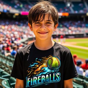 Puede incluir: Una persona lleva una camiseta negra con un gr&aacute;fico de b&eacute;isbol. El gr&aacute;fico presenta una pelota de b&eacute;isbol amarilla con llamas azules y naranjas y la palabra "FIREBALLS" en azul y blanco.