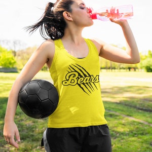 May include: A woman wearing a yellow tank top with the word "Bears" in black lettering and a black claw mark design. She is holding a black soccer ball and drinking from a pink water bottle.