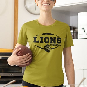 May include: A woman wearing a green t-shirt with a black lion graphic and the text "Lions Football". She is holding a brown football.