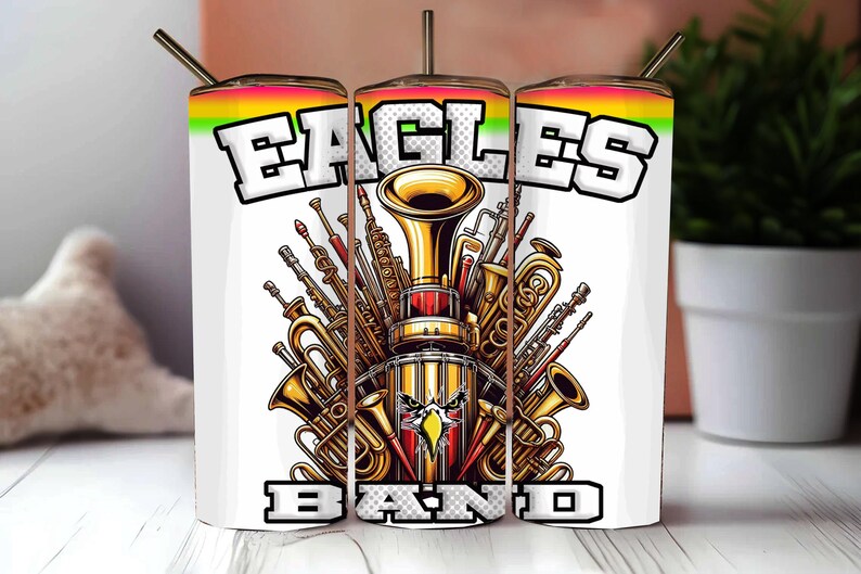 K&ouml;nnte beinhalten: Ein wei&szlig;er Becher mit einem bunten Design mit den Worten "Eagles Band" und einer Grafik von Musikinstrumenten, darunter Trompeten, eine Trommel und eine Tuba.