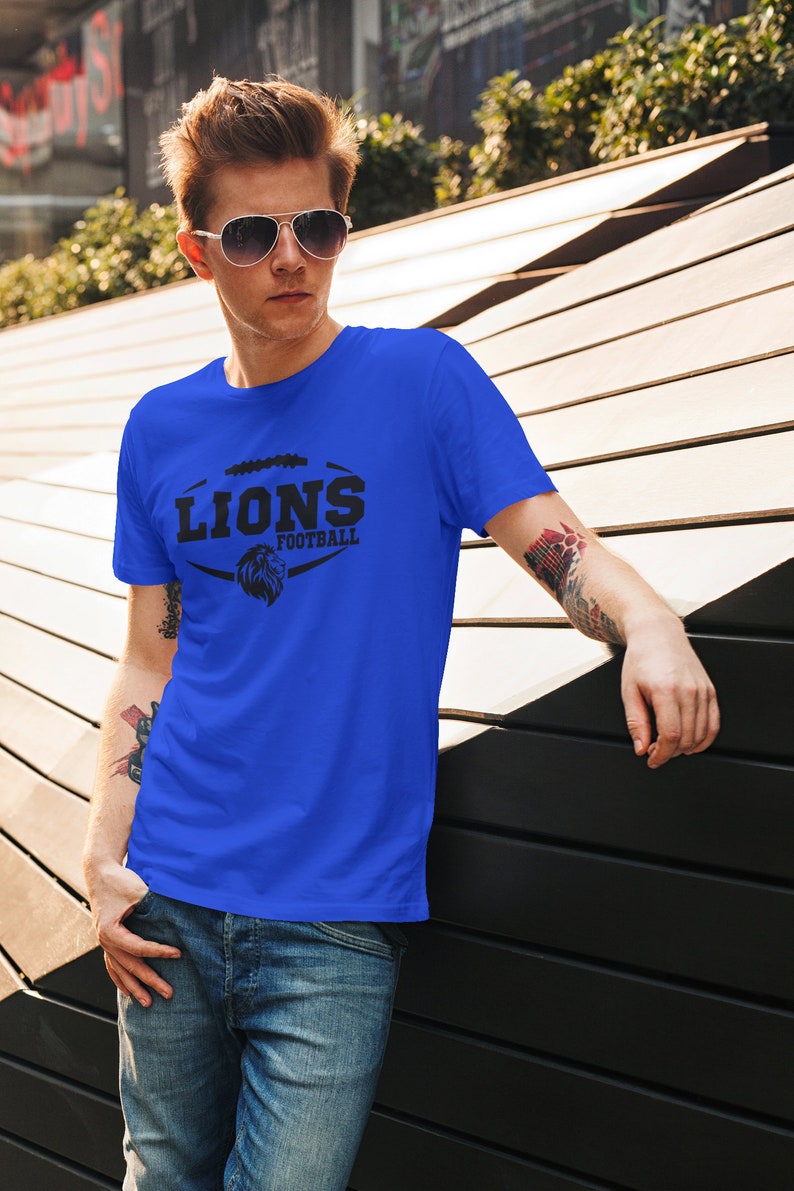 May include: A royal blue t-shirt with a black graphic of a lion's head inside a football. The text "LIONS FOOTBALL" is above the lion's head.