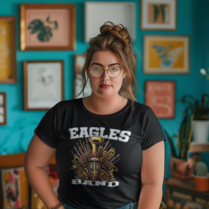 K&ouml;nnte beinhalten: Ein schwarzes T-Shirt mit einem Aufdruck einer Gruppe von Musikinstrumenten, darunter eine Trompete, eine Posaune und eine Klarinette. Der Text "Eagles Band" ist in Wei&szlig; &uuml;ber dem Aufdruck gedruckt.