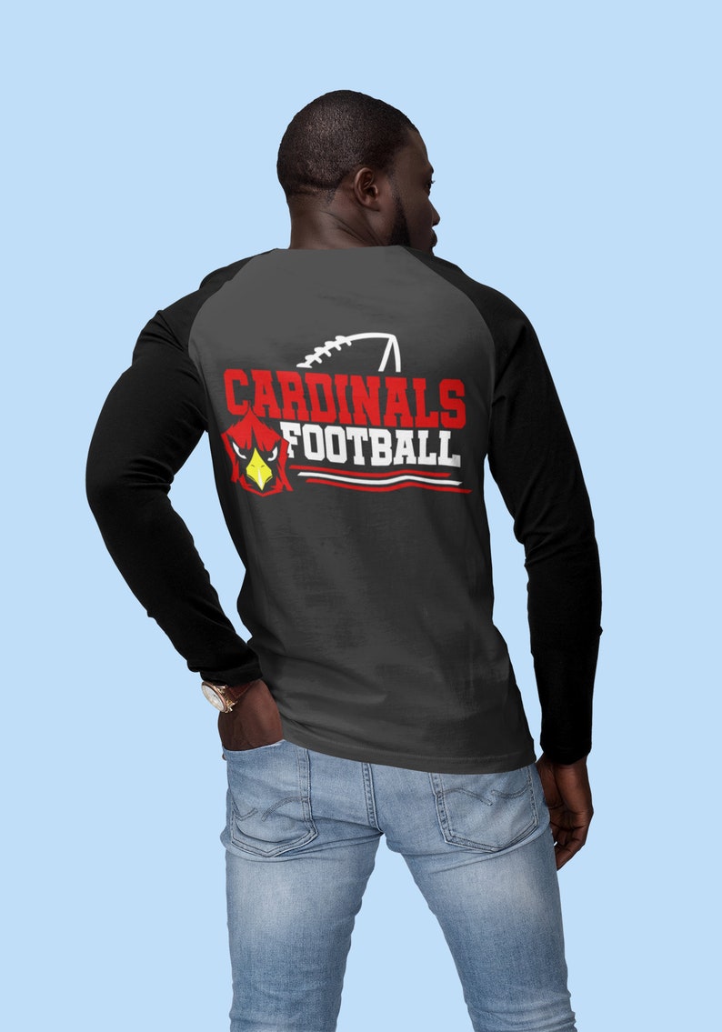 Puede incluir: Una camiseta de manga larga negra y gris con un dise&ntilde;o de estilo b&eacute;isbol en blanco y negro en la espalda. El dise&ntilde;o presenta una cabeza de cardenal roja con las palabras "CARDINALS FOOTBALL" en blanco.