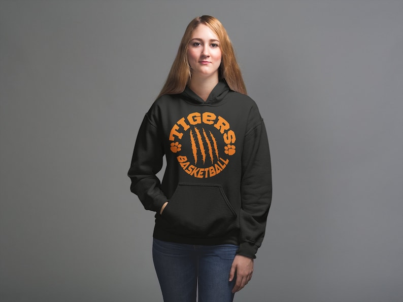 Puede incluir: Sudadera con capucha negra con un gr&aacute;fico circular naranja que dice "Tigers Basketball" con huellas de patas y marcas de garras.