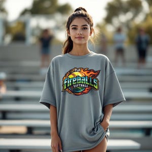 May include: A gray t-shirt with the words "Fireballs Softball" in a colorful design featuring a softball and flames. The shirt is a casual style, with short sleeves.