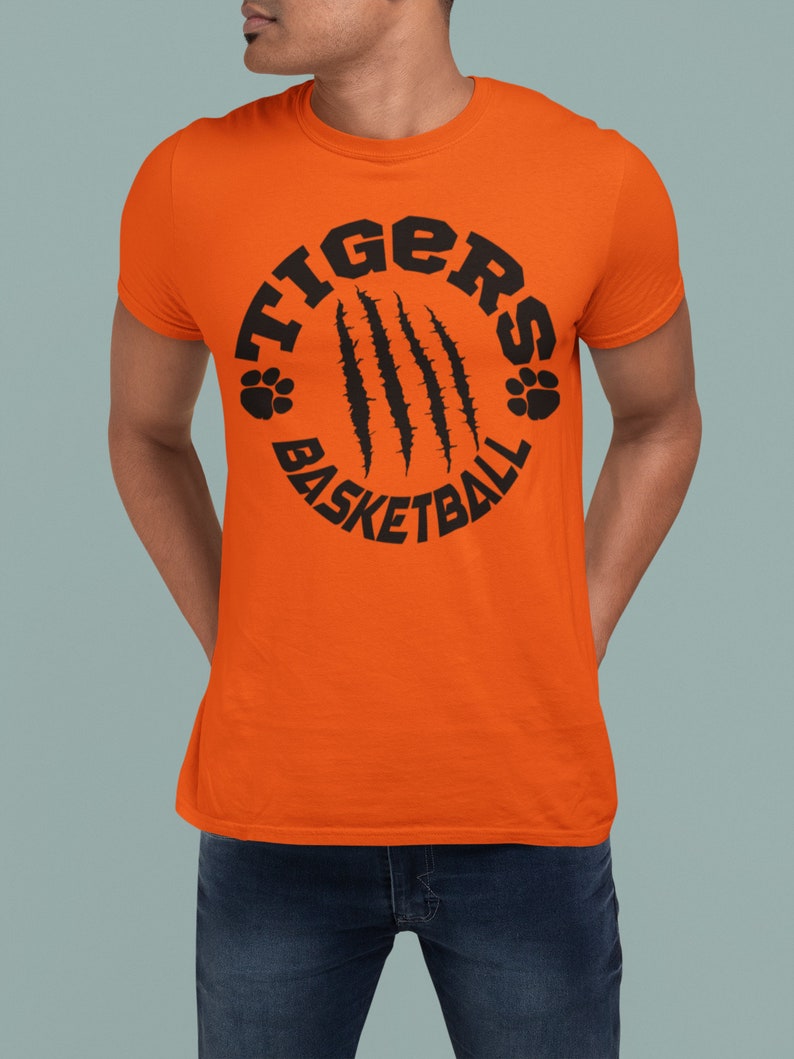 Puede incluir: Camiseta naranja con un gr&aacute;fico circular negro que dice "Tigers Basketball" con huellas de patas y marcas de garras.