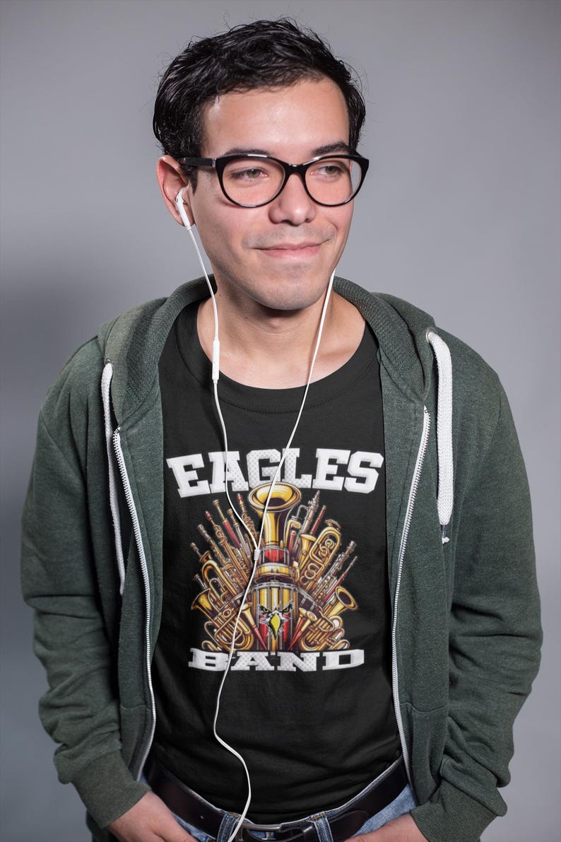 K&ouml;nnte beinhalten: Eine Person tr&auml;gt ein schwarzes T-Shirt mit einer Grafik von Musikinstrumenten und dem Text "Eagles Band". Die Person tr&auml;gt auch einen gr&uuml;nen Kapuzenpullover und hat wei&szlig;e Ohrh&ouml;rer in den Ohren.