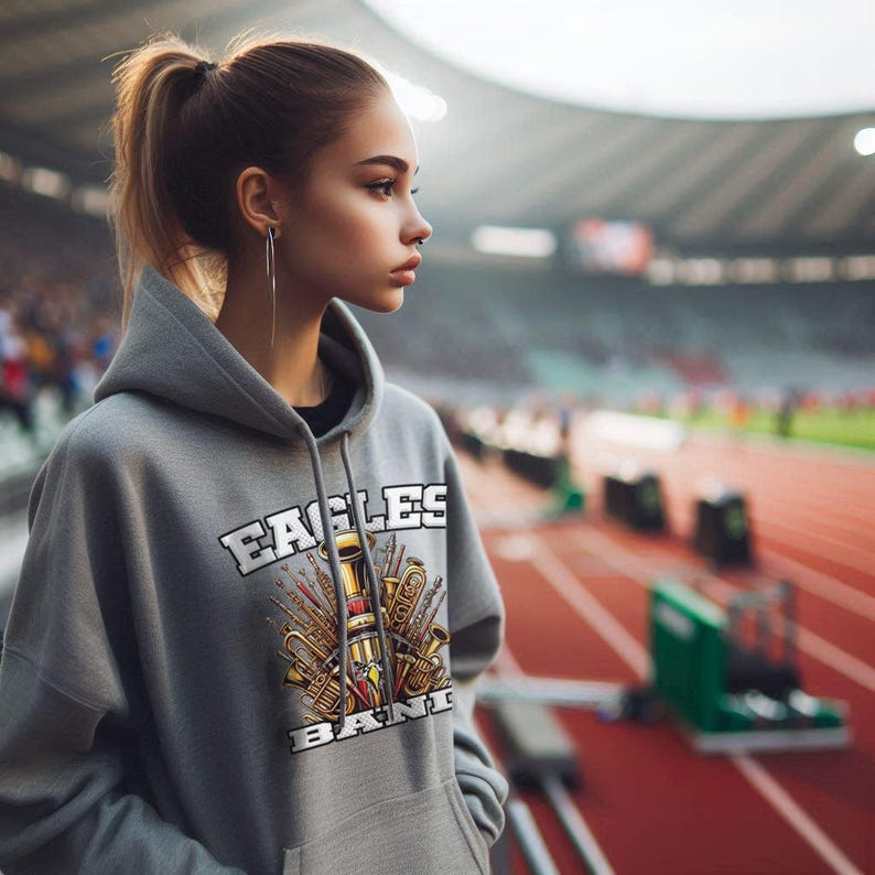 K&ouml;nnte beinhalten: Ein grauer Kapuzenpullover mit dem Text "Eagles Band" und einer Grafik von Musikinstrumenten in Gold und Schwarz.