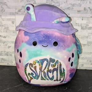 May include: A purple and blue galaxy-print plush toy with a purple hood and a sparkly white patch that says "DREAM".