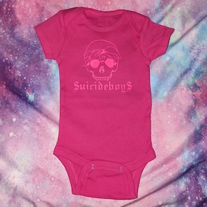 May include: Pink baby onesie with a white skull wearing a bandana with the number 69 on it and the text "Suicideboys" underneath.