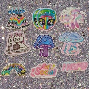 May include: A collection of colorful stickers with various designs. The stickers include images of aliens, mushrooms, cats, rainbows, and text such as "No Bad Trips", "Anti Social", and "NSFW". The stickers have a glittery background.