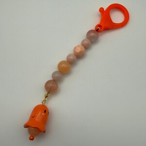 May include: Orange and pink beaded keychain with a small orange ghost charm. The keychain has a bright orange plastic clasp.