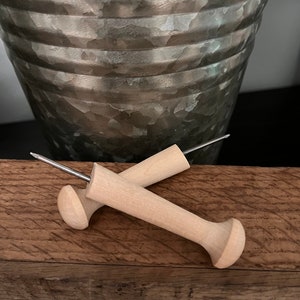 May include: Two wooden dowel rods with metal points, used for hanging items on a wall. The dowels are light brown and the metal points are silver.