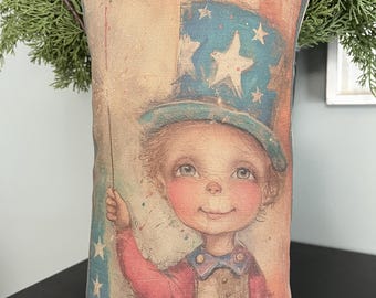 May include: Rectangular decorative pillow featuring a vintage illustration of a child in a patriotic outfit. The child wears a blue top hat with white stars and holds a sparkler. The pillow has a distressed, aged appearance with red, white, and blue colors.