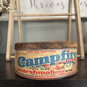 May include: A vintage Campfire marshmallows tin with a patriotic design. The tin features a cartoon marshmallow character wearing a Uncle Sam hat. The text reads "Campfire" in blue letters and "marshmallows" in red. Net weight is 12 oz.