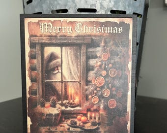 May include: A square wooden Christmas sign with a black border. The sign features a vintage illustration of Santa Claus looking out a window, with the words "Merry Christmas" at the top. Oranges and pinecones decorate the scene.