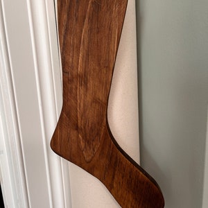 May include: A wooden stocking ornament in a dark brown color. The stocking is hanging from a string.