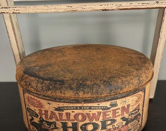 May include: A round metal tin with a distressed, rusted-look lid and a vintage-style Halloween graphic. The side features the text "HALLOWEEN HOP," "TONIGHT'S THE NIGHT!," and "Sweet treats and MOONBEAM NIGHTS," along with illustrations of a black cat and pumpkin.