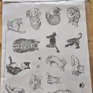 May include: A Mayco Decorating Accessories Cats Silkscreen sheet measuring 18 inches by 12 inches. The white sheet features various black ink illustrations of cats in different poses, including a cat with a ball of yarn and a speech bubble with the text meow.