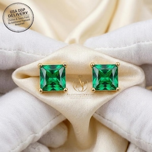 May include: Two square emerald-cut green gemstone stud earrings with gold settings. The earrings are presented on a cream-coloured fabric. The image includes the text "USA DDP DELIVERY" and "ALLSTONE JEWELRY".