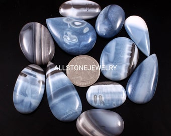 May include: A collection of polished blue and white opal gemstones in various shapes, including oval and teardrop. The stones display unique patterns and swirls. The image includes a quarter for size reference. The text "ALLSTONE JEWELRY" is visible.